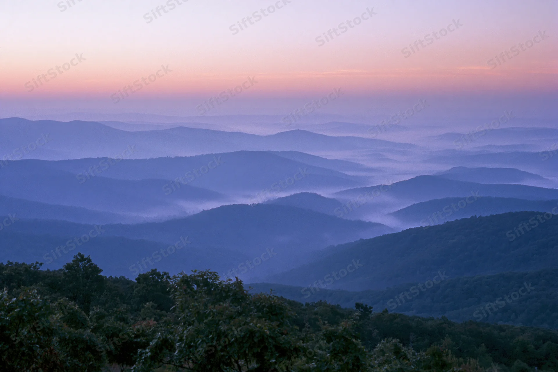 Layered appalachian mountain ridges receding into the distance under a soft dawn sky with mist in the valleys