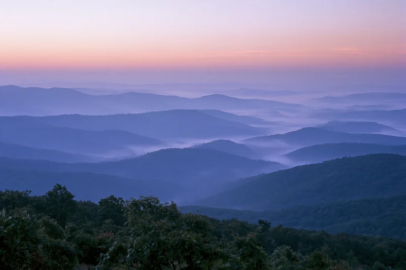 Layered appalachian mountain ridges receding into the distance under a soft dawn sky with mist in the valleys