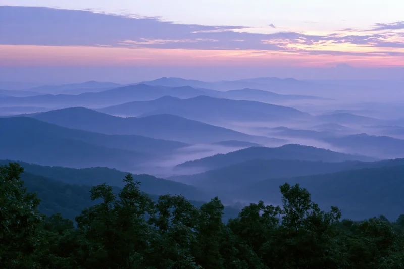 Layered appalachian mountain ridges receding into the distance under a hazy dawn sky with mist in the valleys