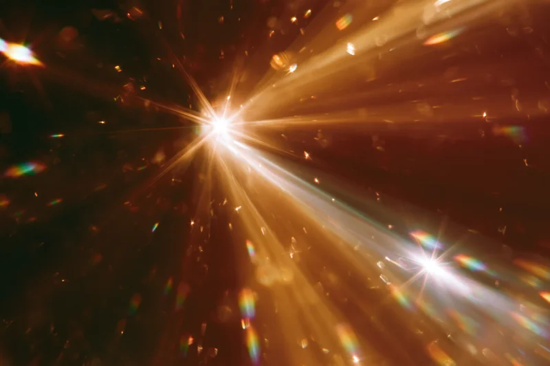 Light refracting through crystal surface creating starburst and rainbow flares in dark background