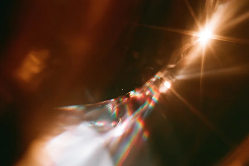 Light refracting through a glass crystal held close, creating a rainbow spectrum against a dark background
