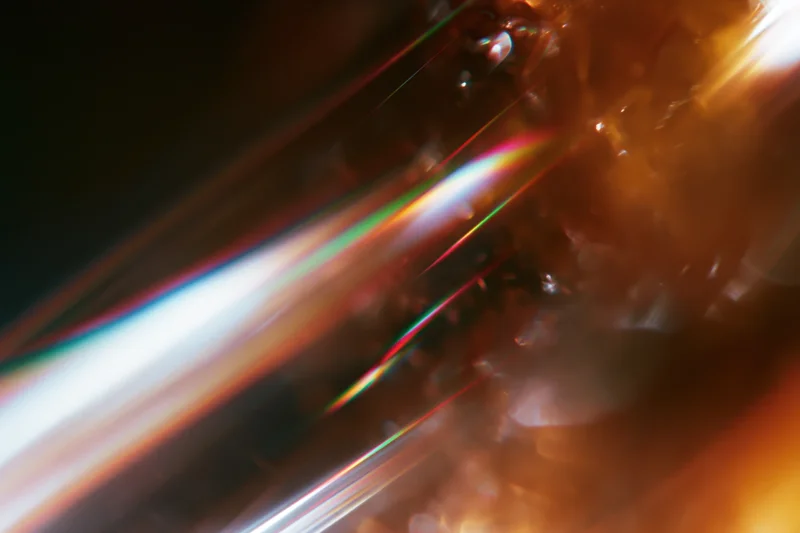 Light refracting through a glass crystal held close, creating a rainbow spectrum on a warm-toned surface