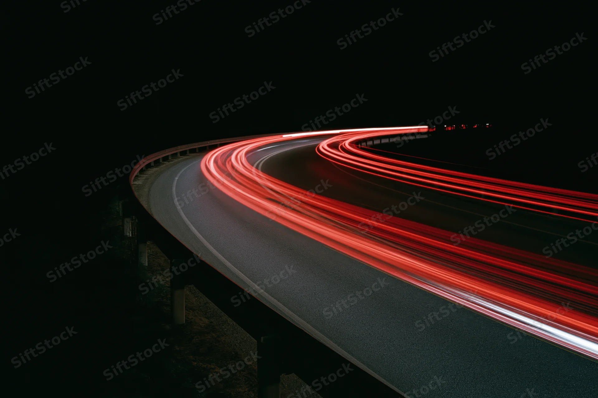 Curved highway at night with red taillight trails from moving vehicles