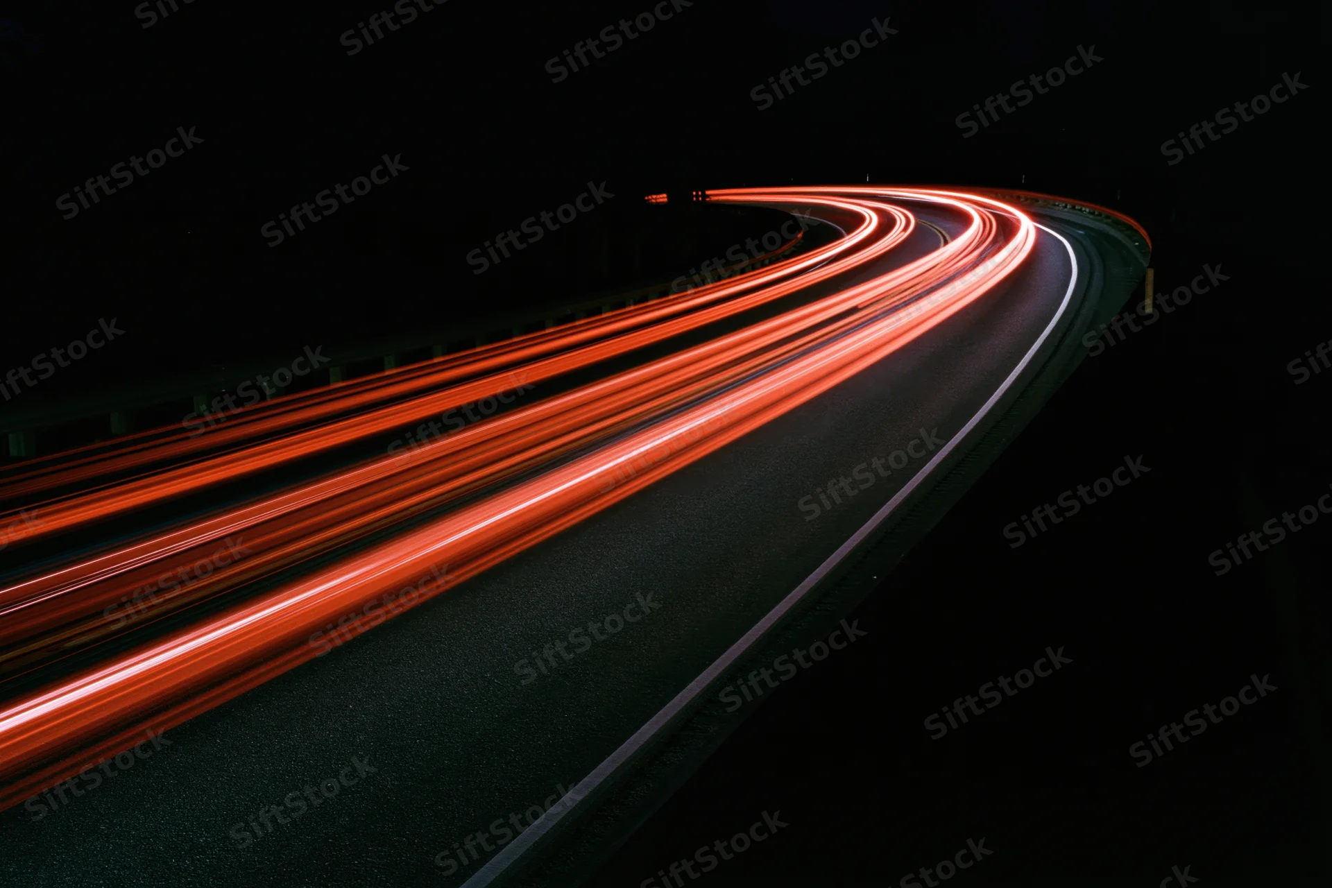 Curved highway at night with red taillight streaks from moving vehicles