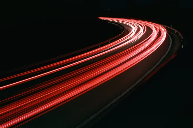 Red taillight streaks from vehicles moving along a curved highway at night