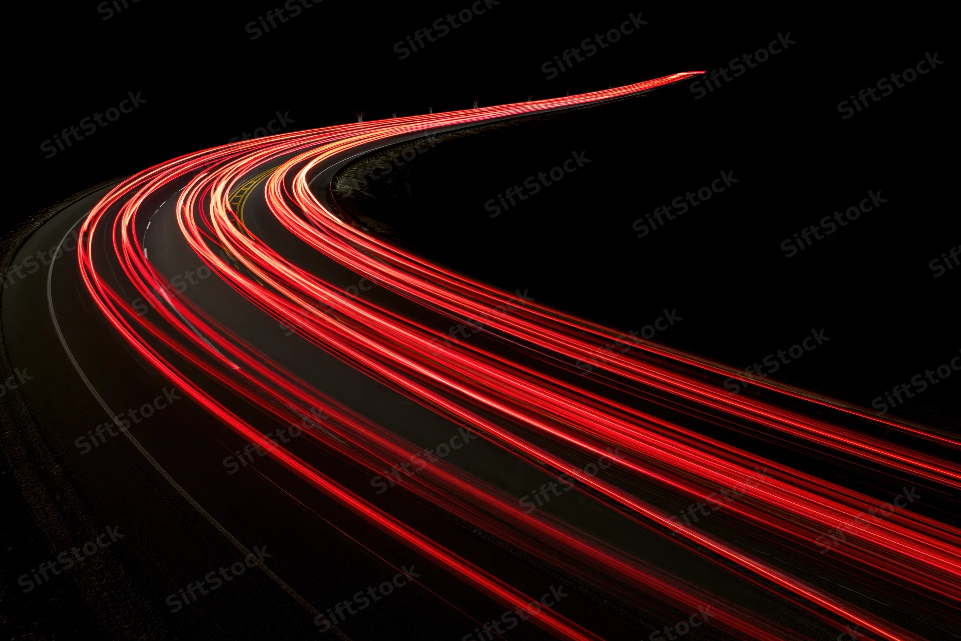 Red tail light streaks tracing a curving highway at night