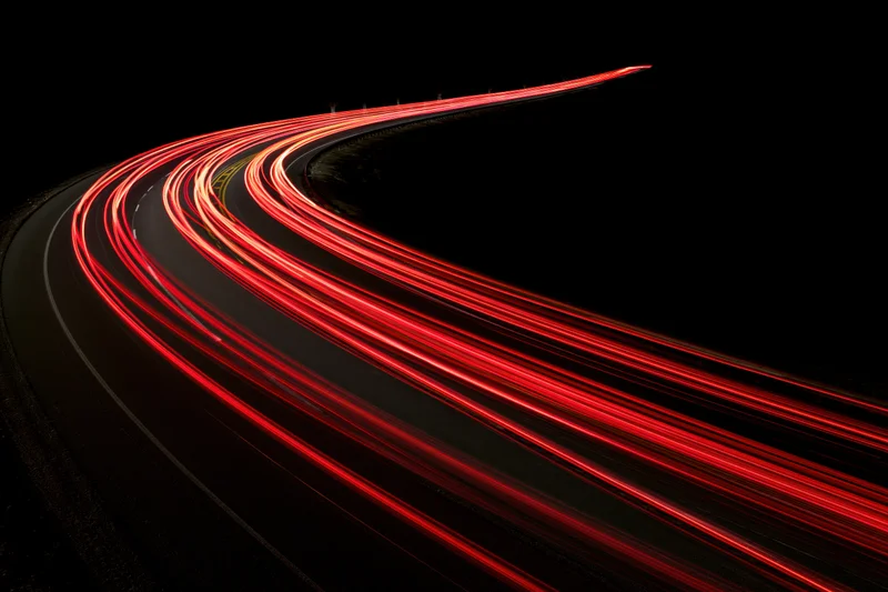 Red tail light streaks tracing a curving highway at night