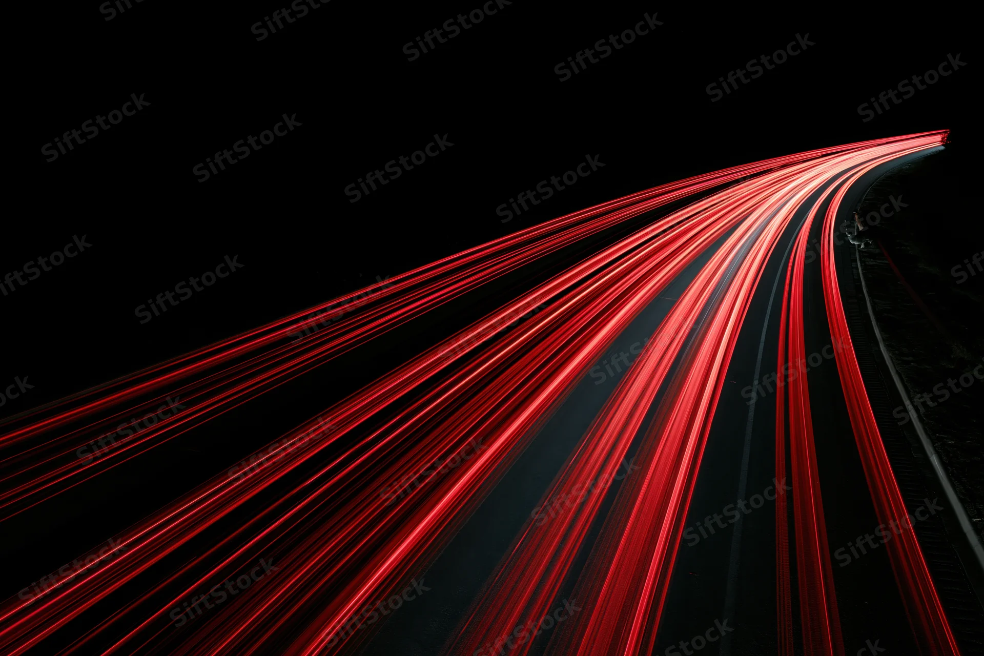 Curving highway at night with red tail light streaks from moving vehicles