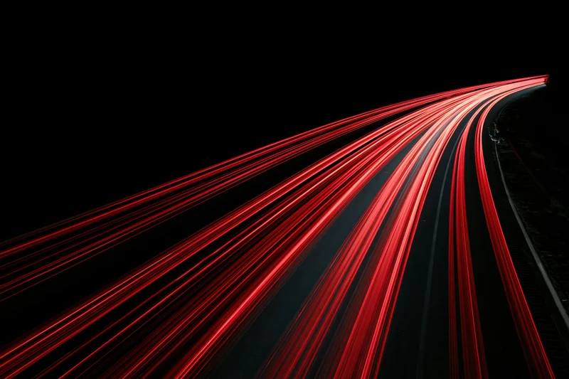 Curving highway at night with red tail light streaks from moving vehicles