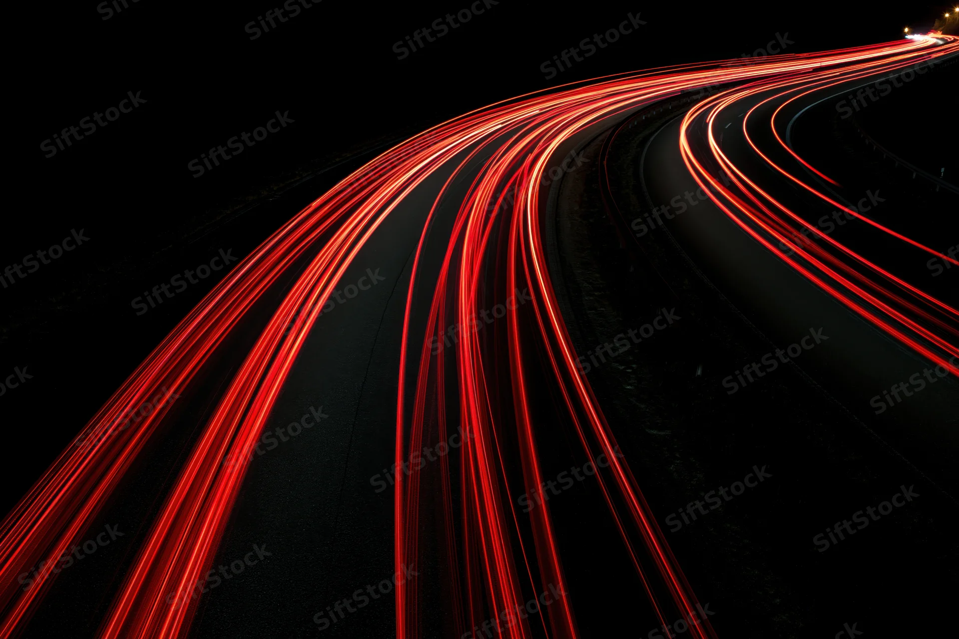 Curving highway at night with red tail light streaks from moving vehicles