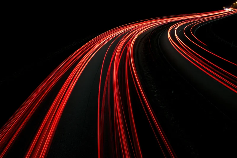 Curving highway at night with red tail light streaks from moving vehicles