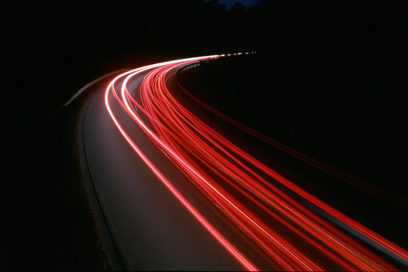 Red light trails from vehicles moving along a curved highway at night
