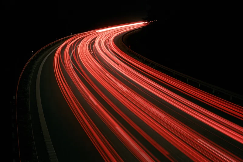 Red taillight streaks from vehicles moving along a curved highway at night