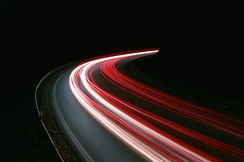 Long-exposure night view of curved highway with red and white light trails from moving vehicles