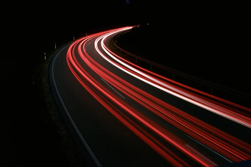 Long-exposure night view of curved highway with red and white light trails from moving vehicles