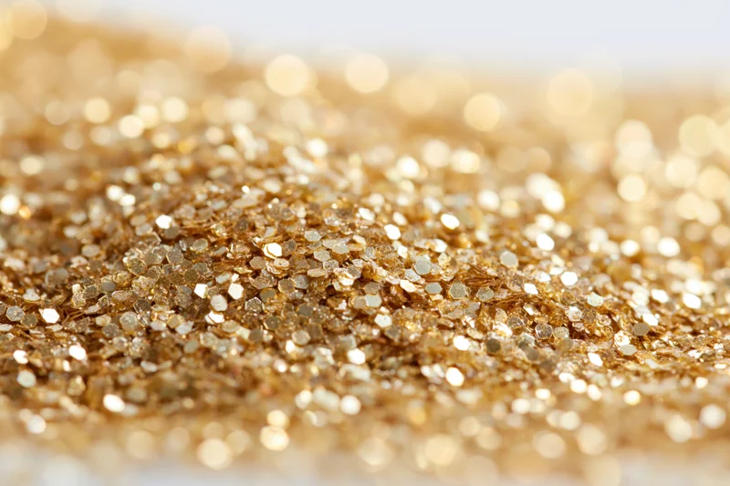 Scattered gold glitter and sequins in macro closeup on a flat surface with bokeh background