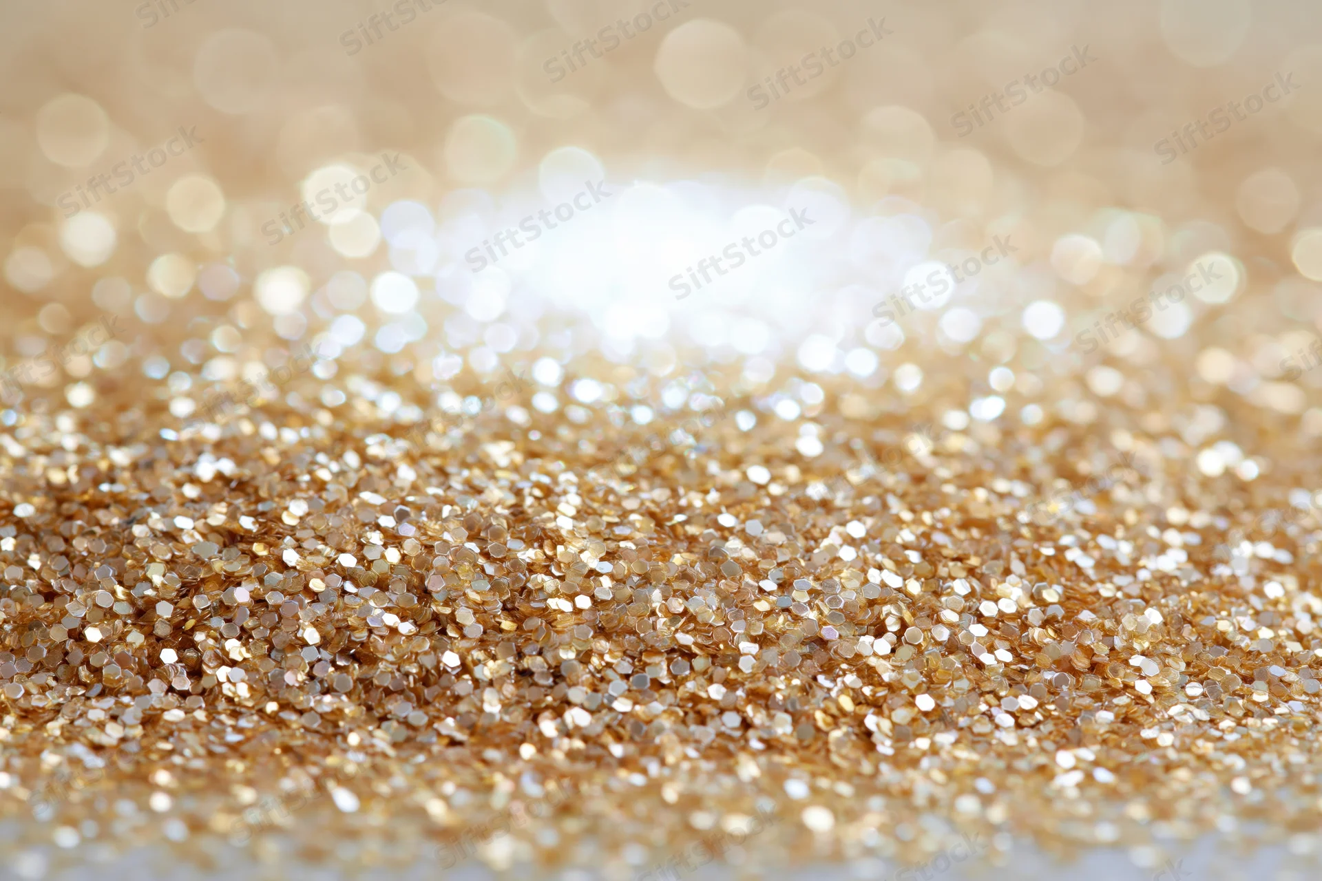 Scattered gold glitter and sequins on a flat surface with bokeh background