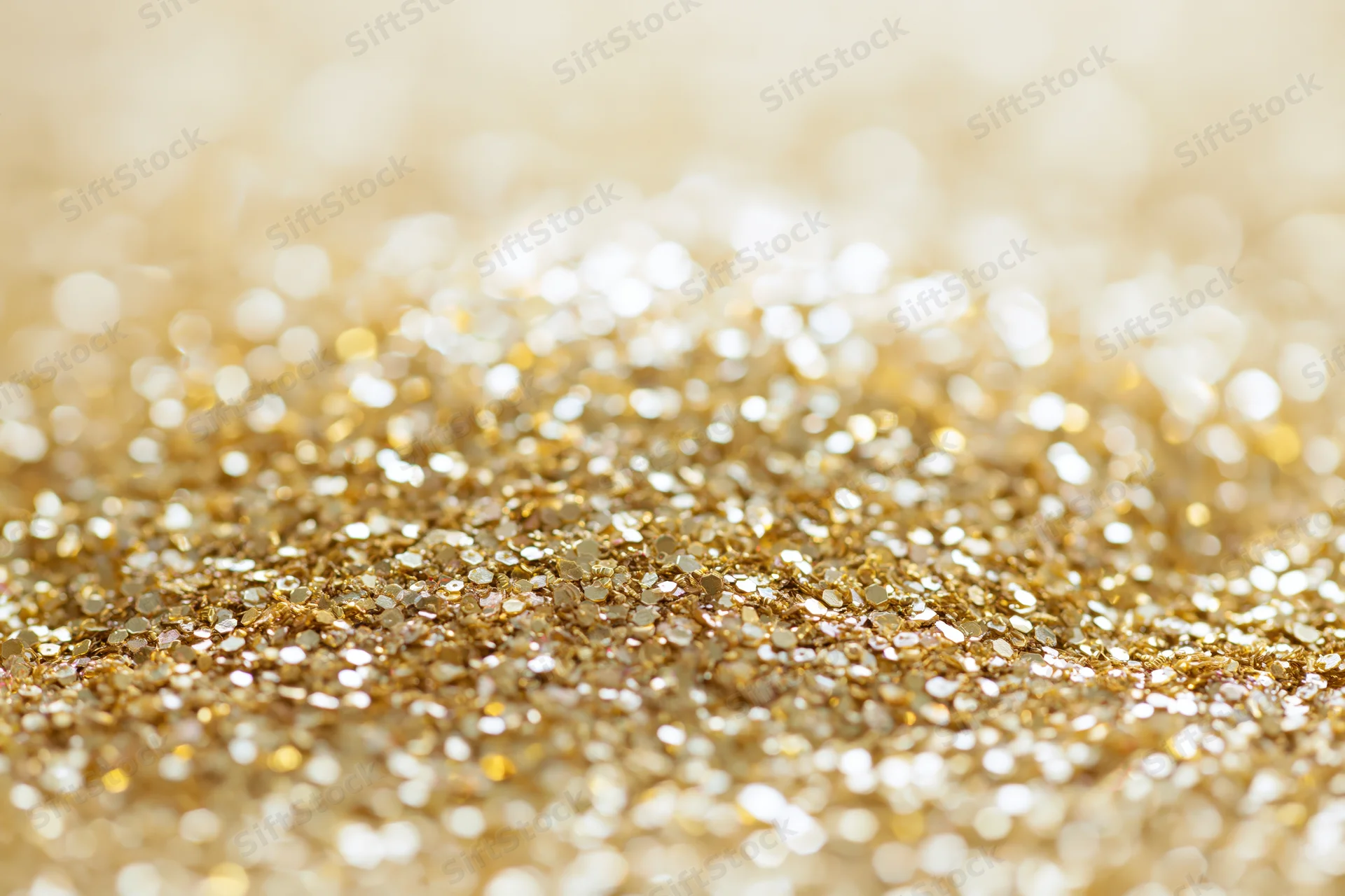 Scattered gold glitter and sequins on a flat surface with bokeh highlights