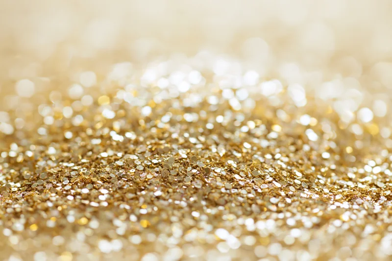 Scattered gold glitter and sequins on a flat surface with bokeh highlights