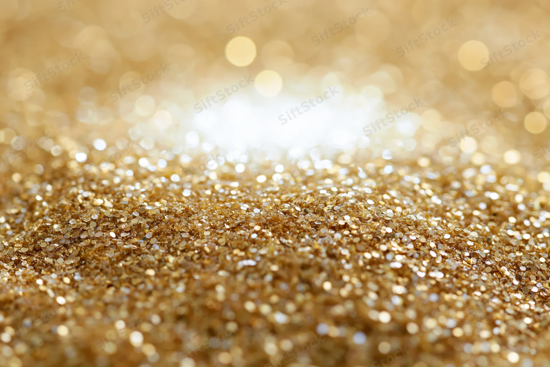 Scattered gold glitter and sequins on a flat surface with bokeh background