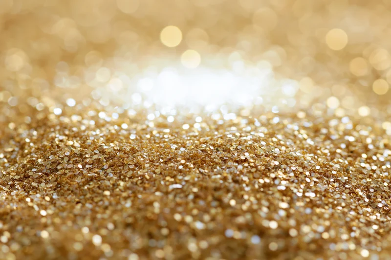Scattered gold glitter and sequins on a flat surface with bokeh background