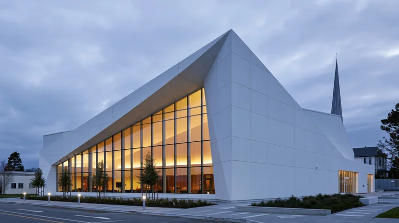 Modern white church with angular glass facade and spire at evening