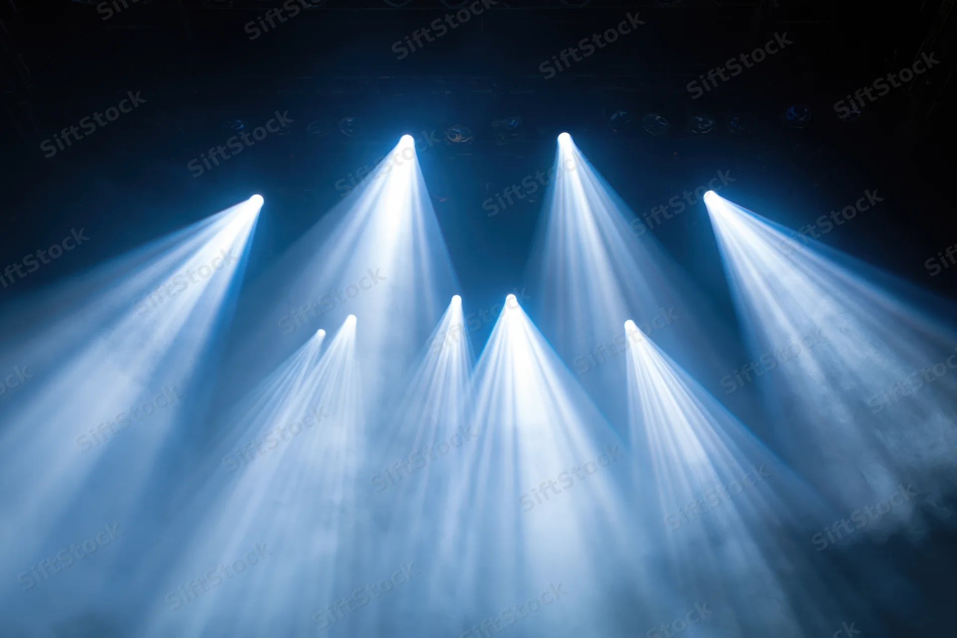 Multiple spotlights shining upward through haze in a dark theater setting