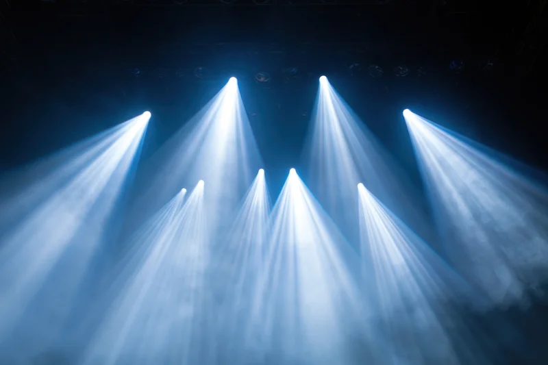 Multiple spotlights shining upward through haze in a dark theater setting