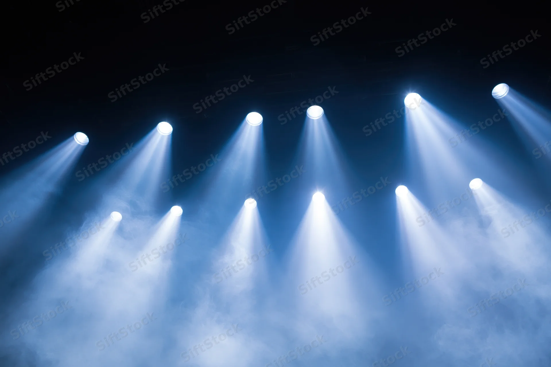 Multiple spotlights shining upward through haze in a dark stage setting