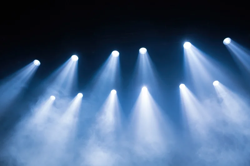 Multiple spotlights shining upward through haze in a dark stage setting
