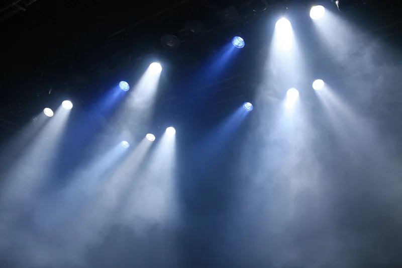 Multiple stage spotlights casting bright white and blue beams through smoke in a dark venue