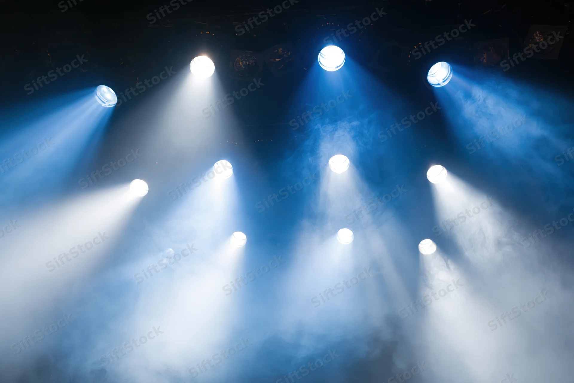 Multiple stage spotlights casting bright white and blue beams through smoke in a theater setting