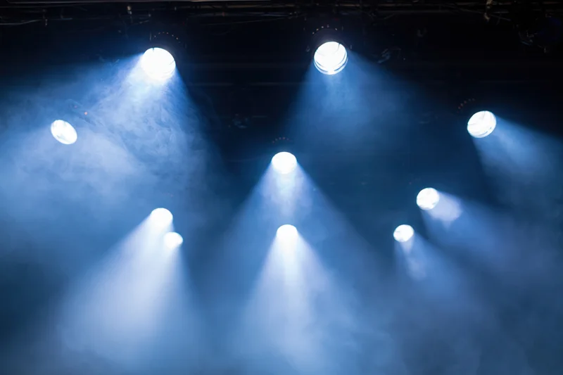 Multiple stage spotlights casting bright white and blue beams through smoke in a theater setting
