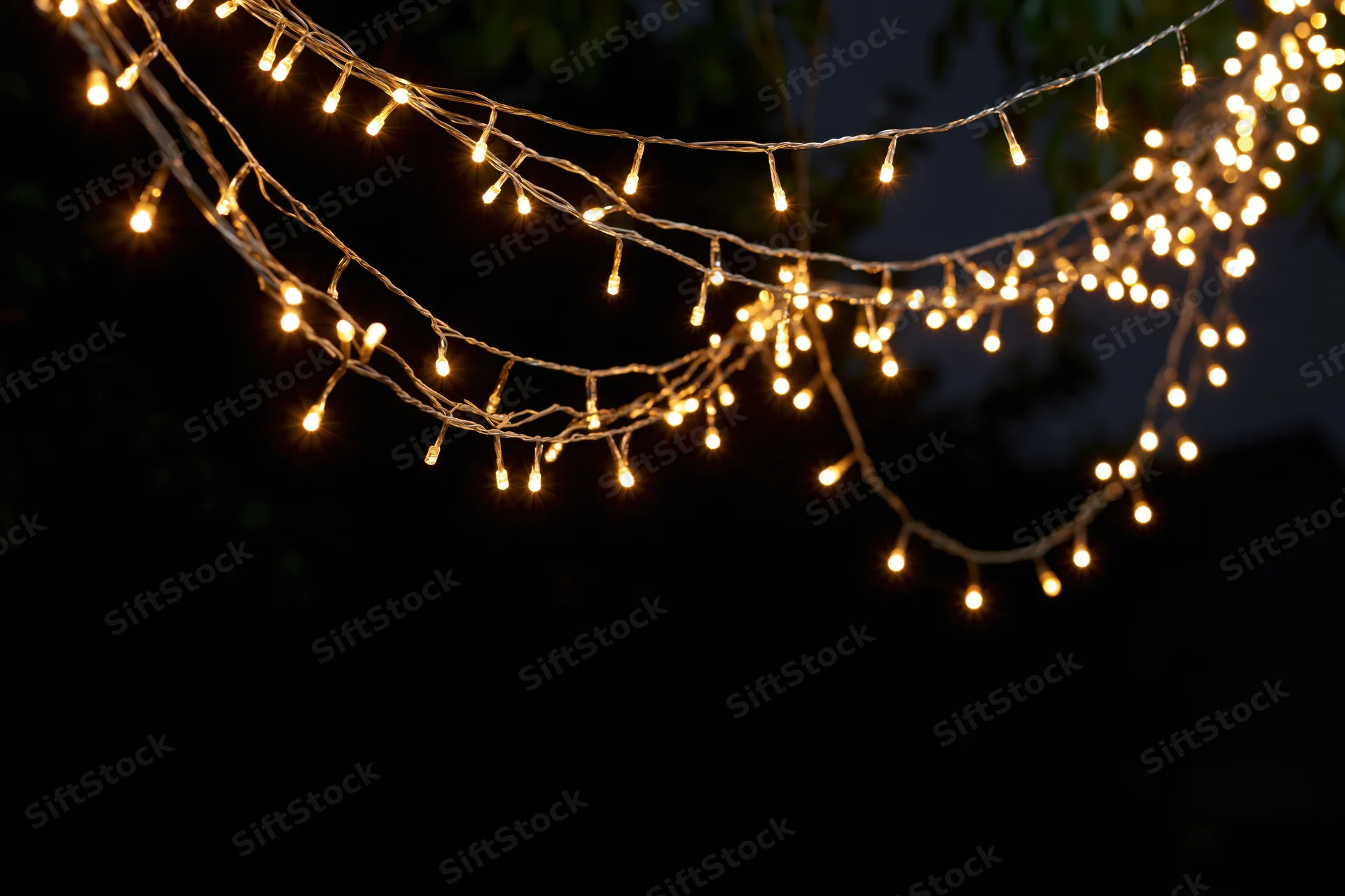 Multiple strands of warm white fairy lights draped loosely across a dark outdoor space at night