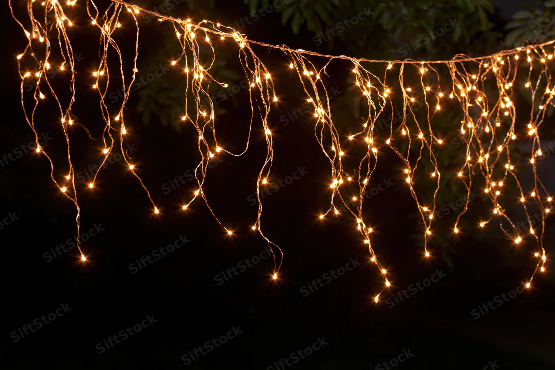 Multiple strands of warm white fairy lights draped loosely across a dark outdoor space at night