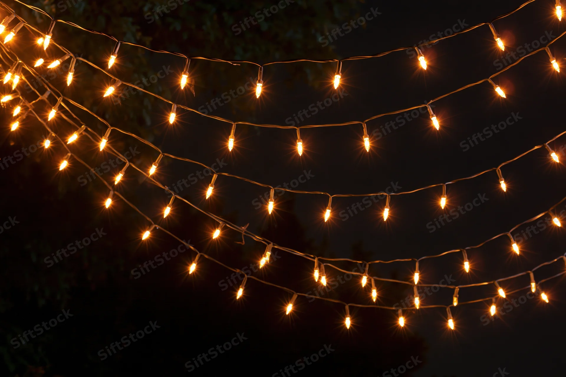 Multiple strands of warm white fairy lights draped loosely across a dark outdoor space at night