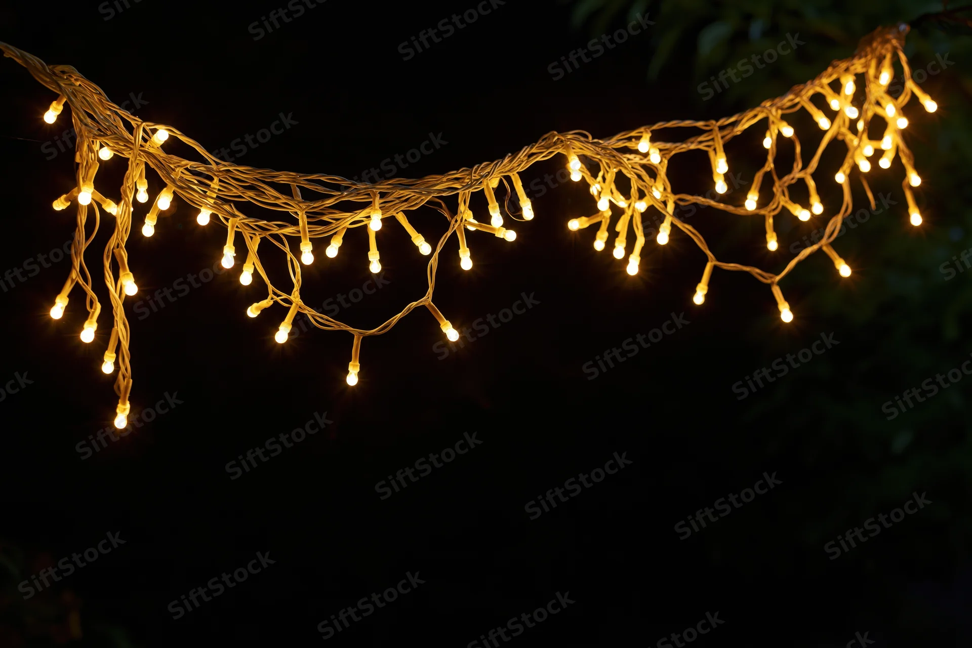 Multiple strands of warm yellow fairy lights draped loosely against a dark background at night
