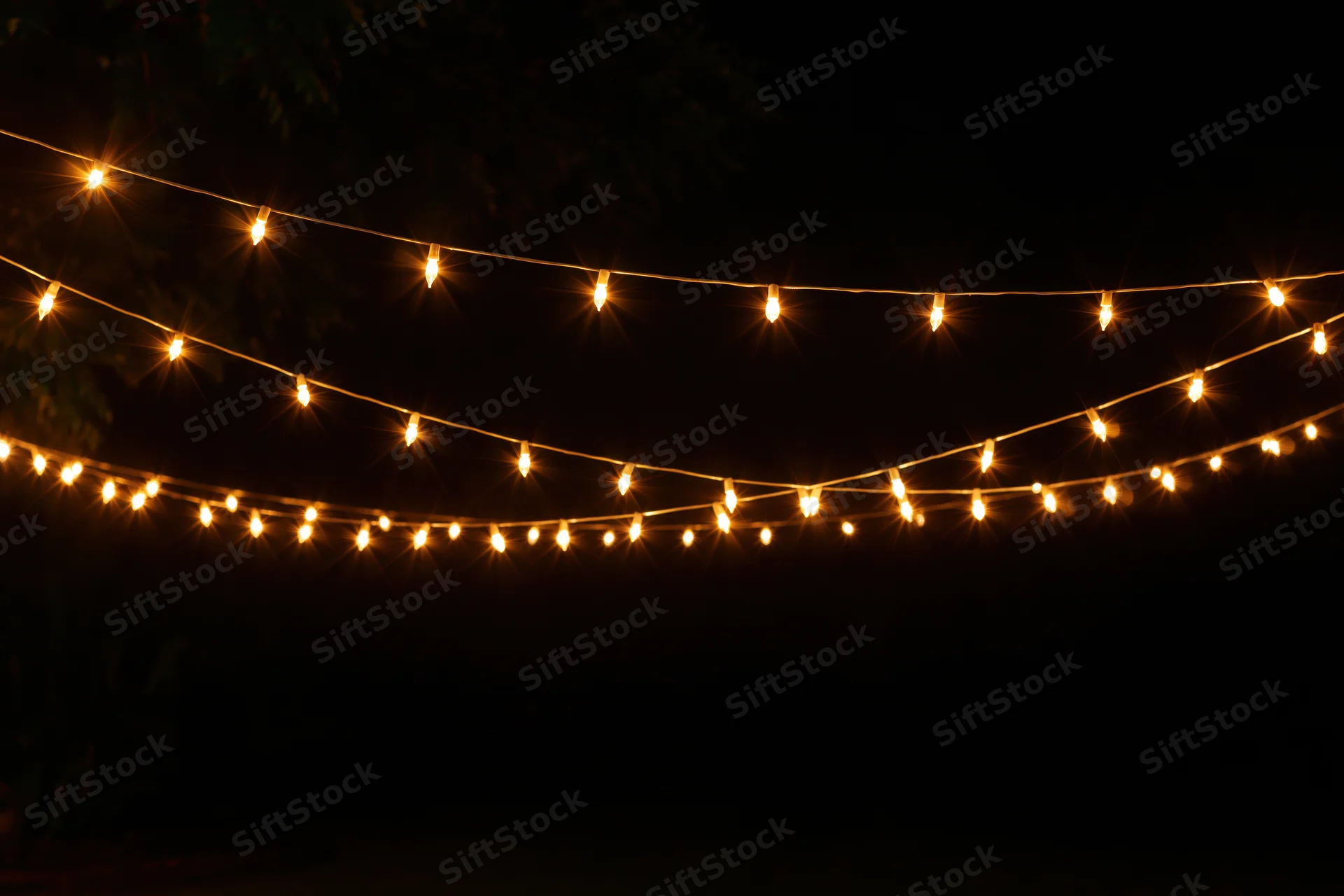 Multiple strands of warm yellow fairy lights draped loosely against a dark night sky in an outdoor setting