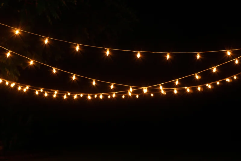 Multiple strands of warm yellow fairy lights draped loosely against a dark night sky in an outdoor setting