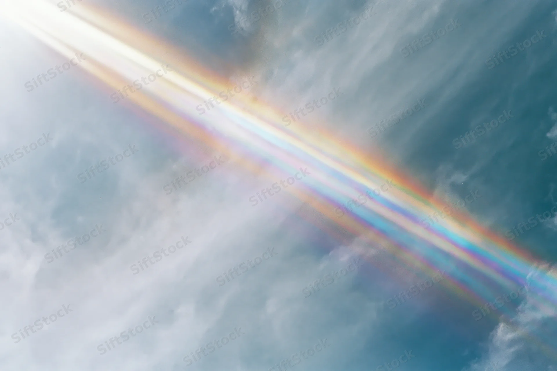 Overexposed pale blue sky with wispy clouds and a lens prism rainbow effect