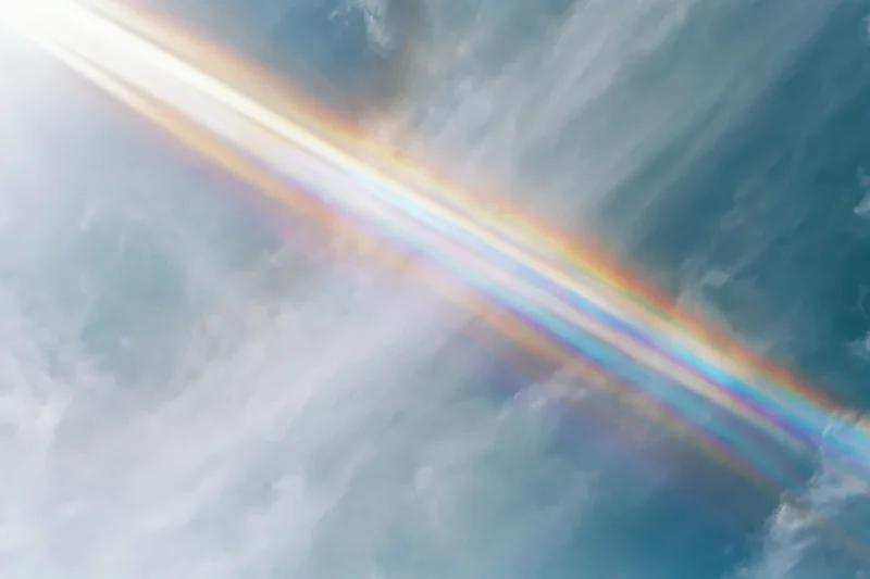 Overexposed pale blue sky with wispy clouds and a lens prism rainbow effect
