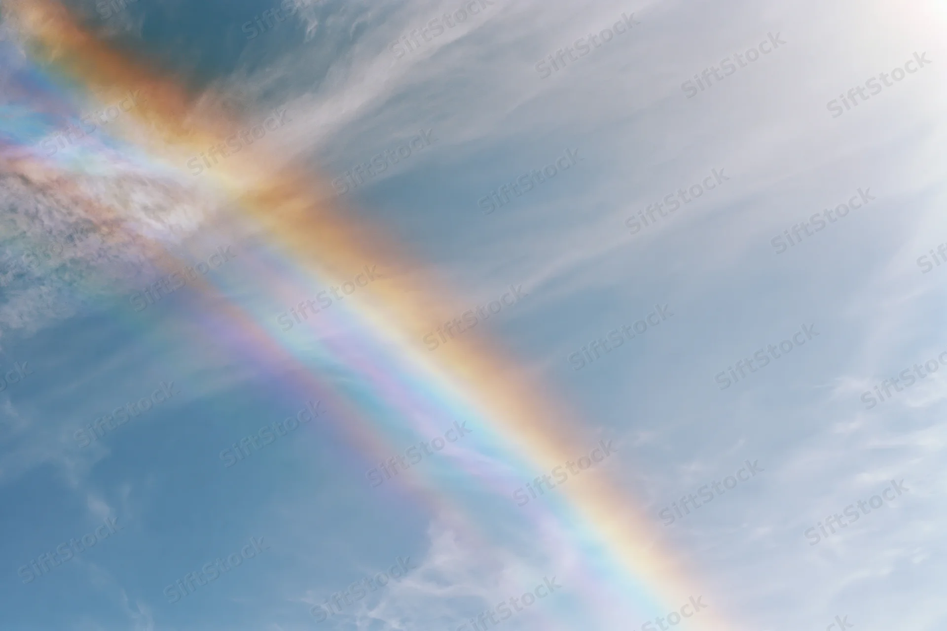 Pale blue sky with wispy clouds and a diagonal iridescent rainbow effect from light refraction