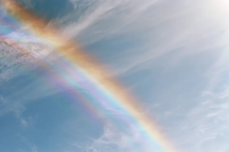 Pale blue sky with wispy clouds and a diagonal iridescent rainbow effect from light refraction