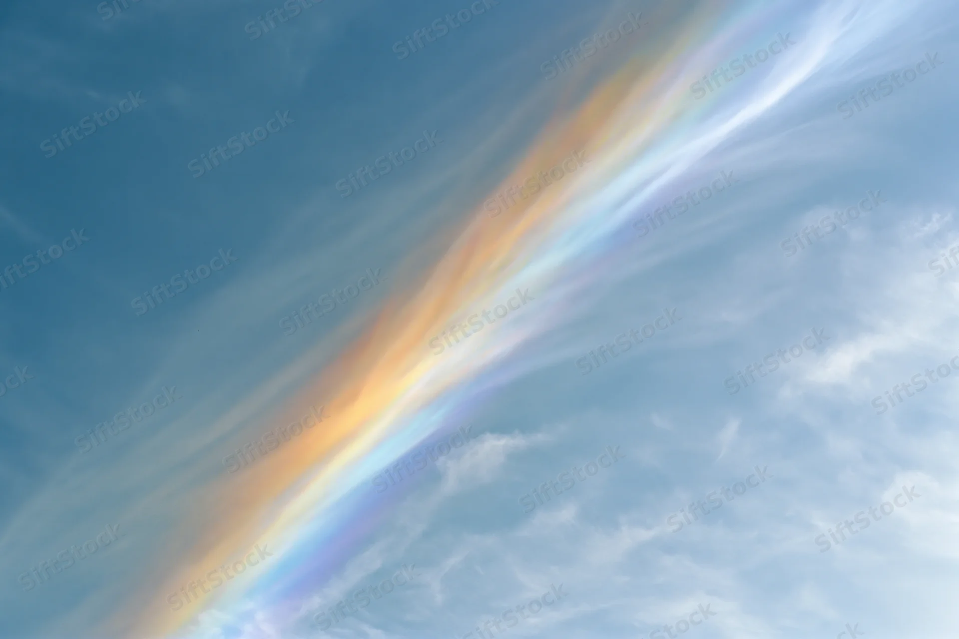Iridescent rainbow arc across pale blue sky with wispy cirrus clouds