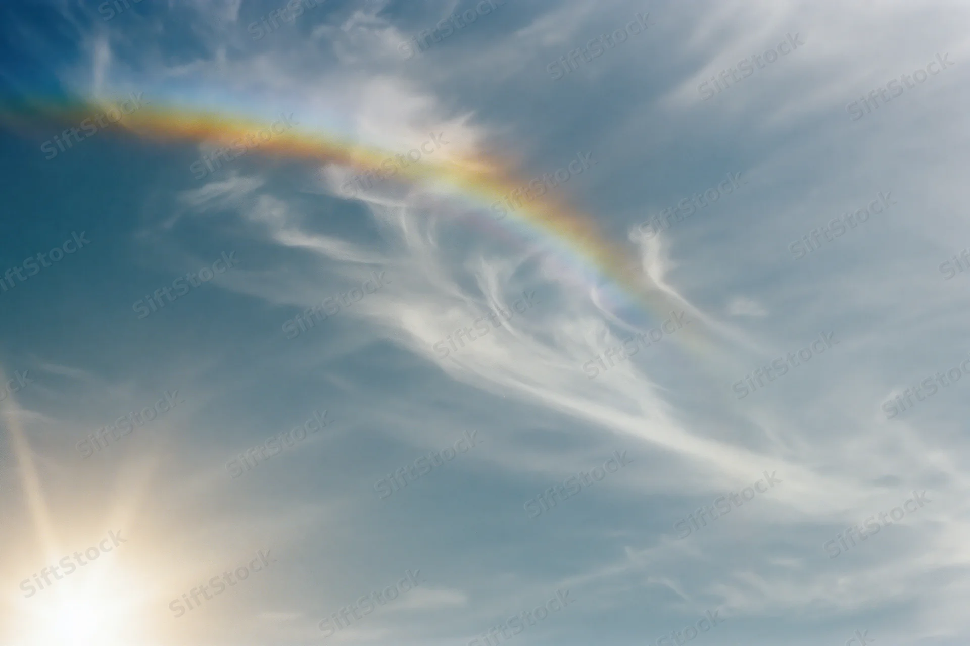 Overexposed sky with wispy cirrus clouds and a faint rainbow arc near the sun