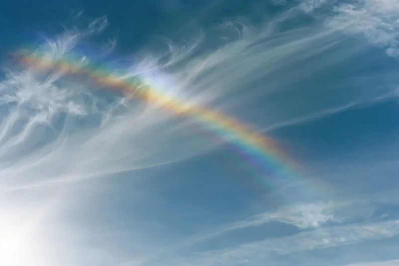 Rainbow arcing across overexposed sky with wispy cirrus clouds