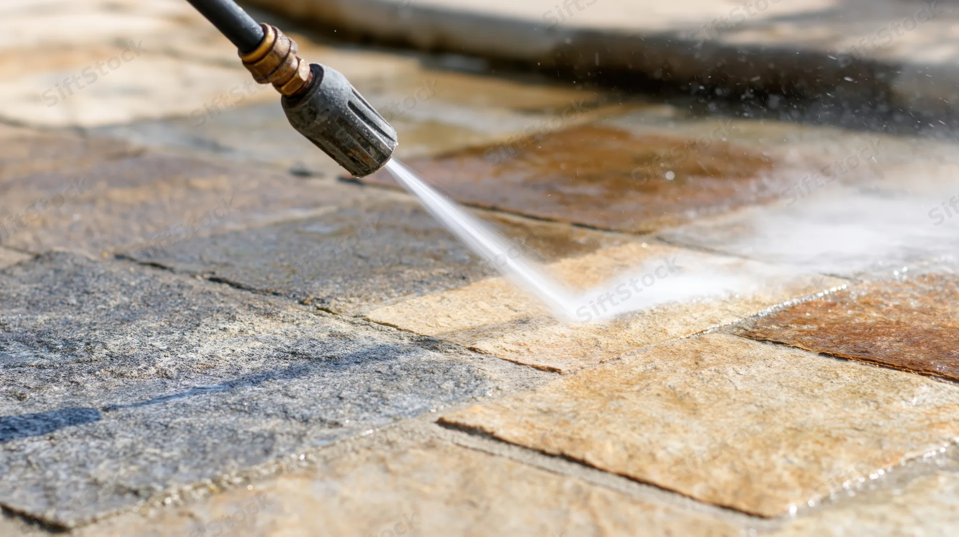 Pressure washer lance spraying water onto stone patio tiles for cleaning