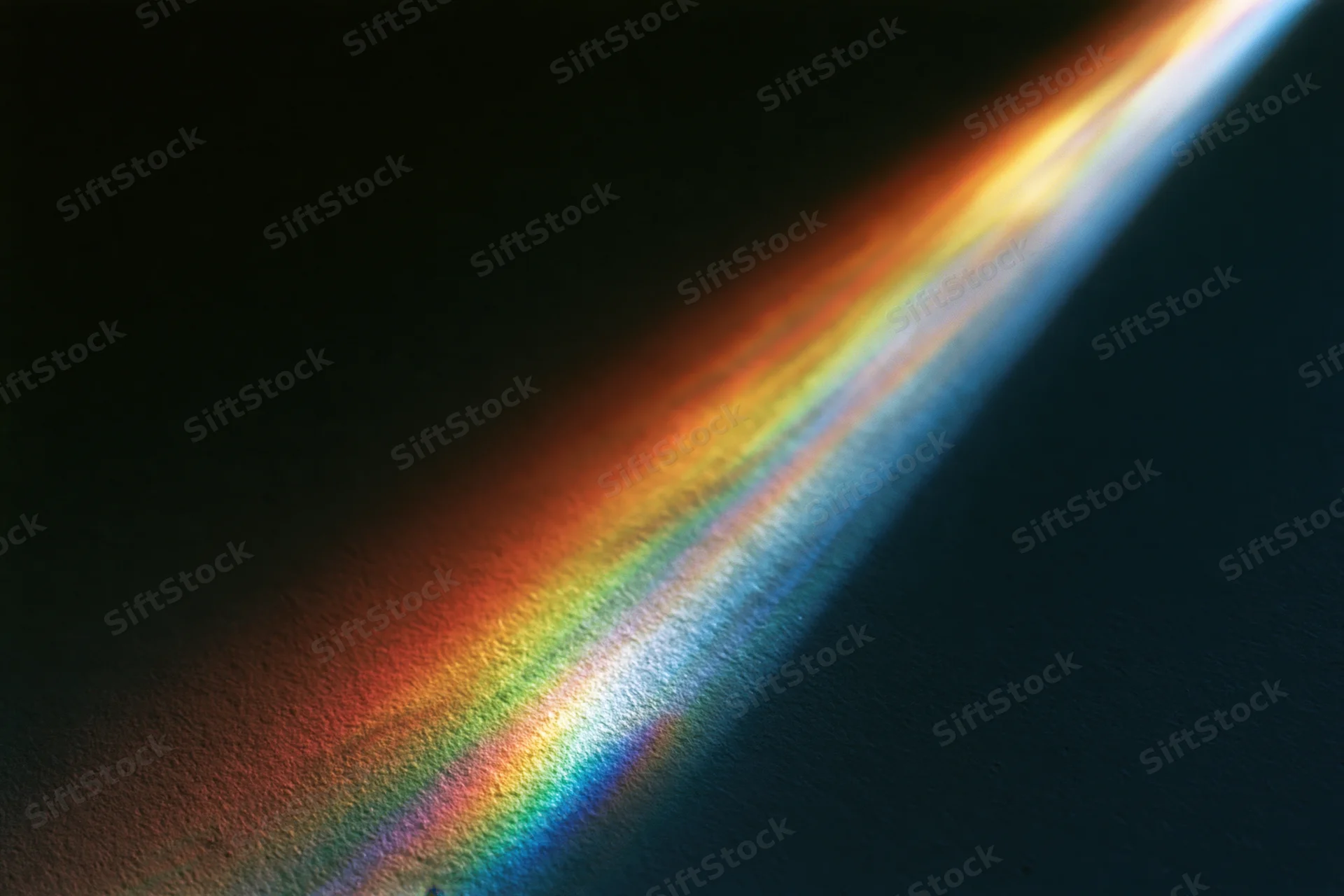 Prismatic light refraction casting a spectrum arc across a dark surface