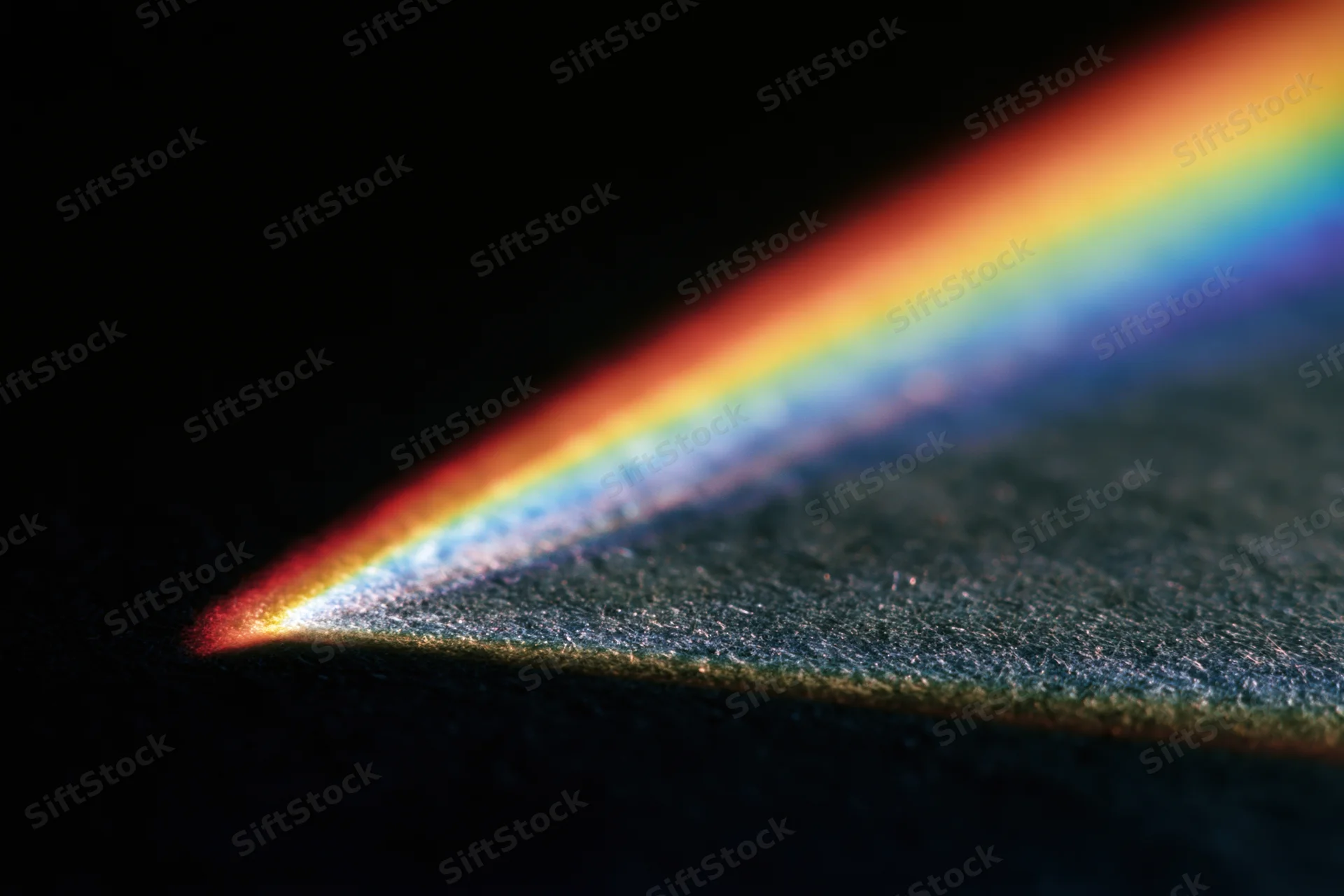 Prismatic light refracting into a rainbow spectrum across a dark textured surface