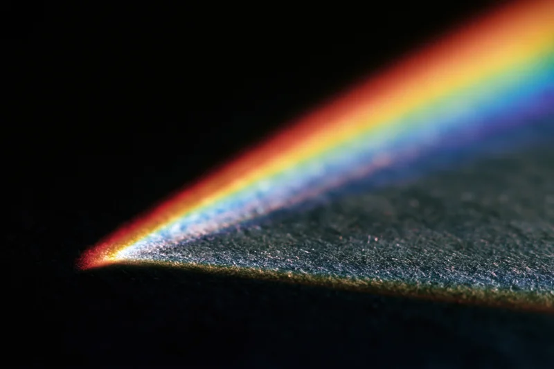 Prismatic light refracting into a rainbow spectrum across a dark textured surface